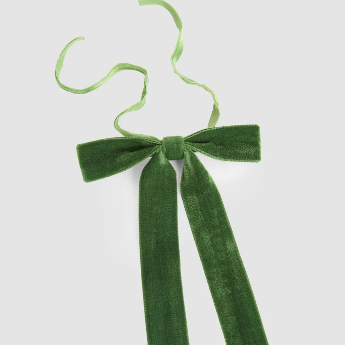 Close-up of a green velvet tie-on bow showing the ribbon texture, central knot and narrow tying ribbons