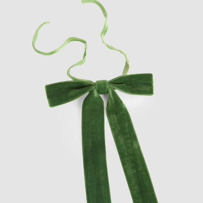 Close-up of a green velvet tie-on bow showing the ribbon texture, central knot and narrow tying ribbons