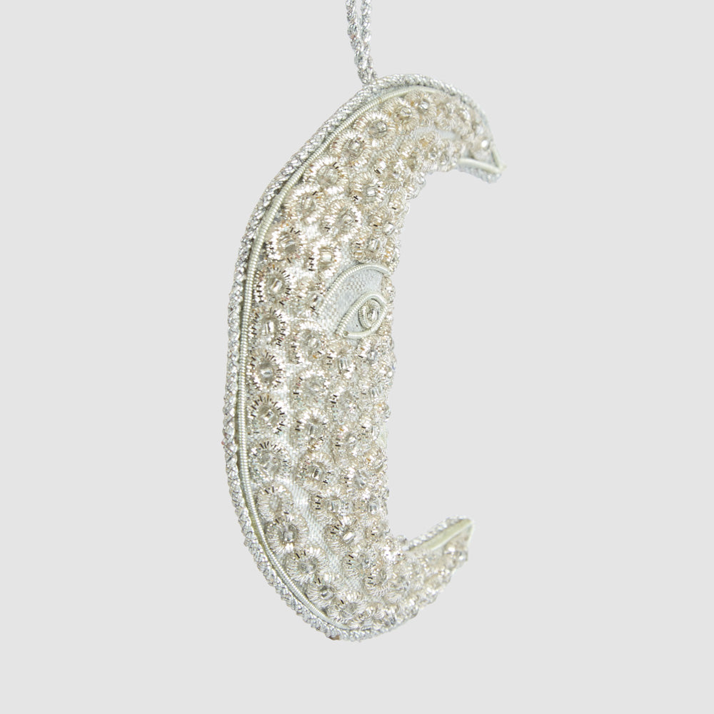 Angled view of the silver moon face decoration showing its slim profile and decorative edging