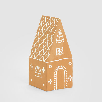 Tan paper mache gingerbread house with a steep pitched roof and white painted door and windows