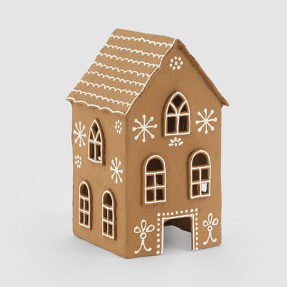 Tall tan paper mache gingerbread house with white scalloped roof lines, cut-out windows and open doorway