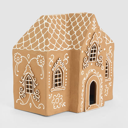 Large tan paper mache gingerbread house with white floral decoration, ornate windows and arched doorway