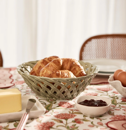 Light green woven ceramic bowl filled with croissants on a floral breakfast table
