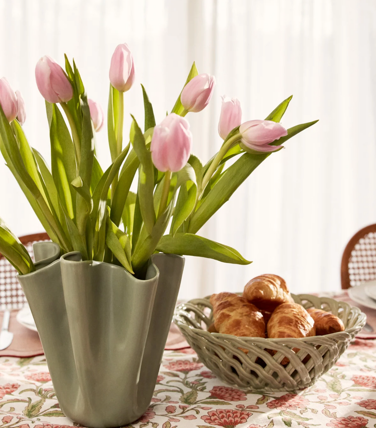 Light green lattice ceramic bowl holding croissants beside a vase of pink tulips