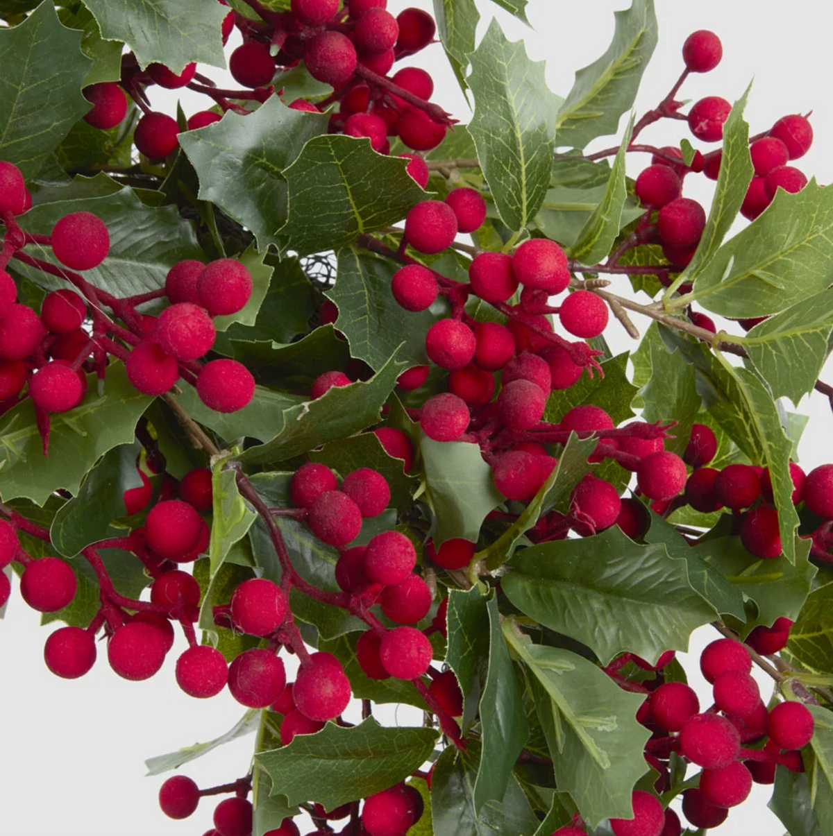 Close-up of the wreath showing veined green holly leaves and red artificial berries