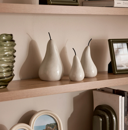 Off white ceramic pear sculptures arranged on a shelf beside a green vase and framed picture