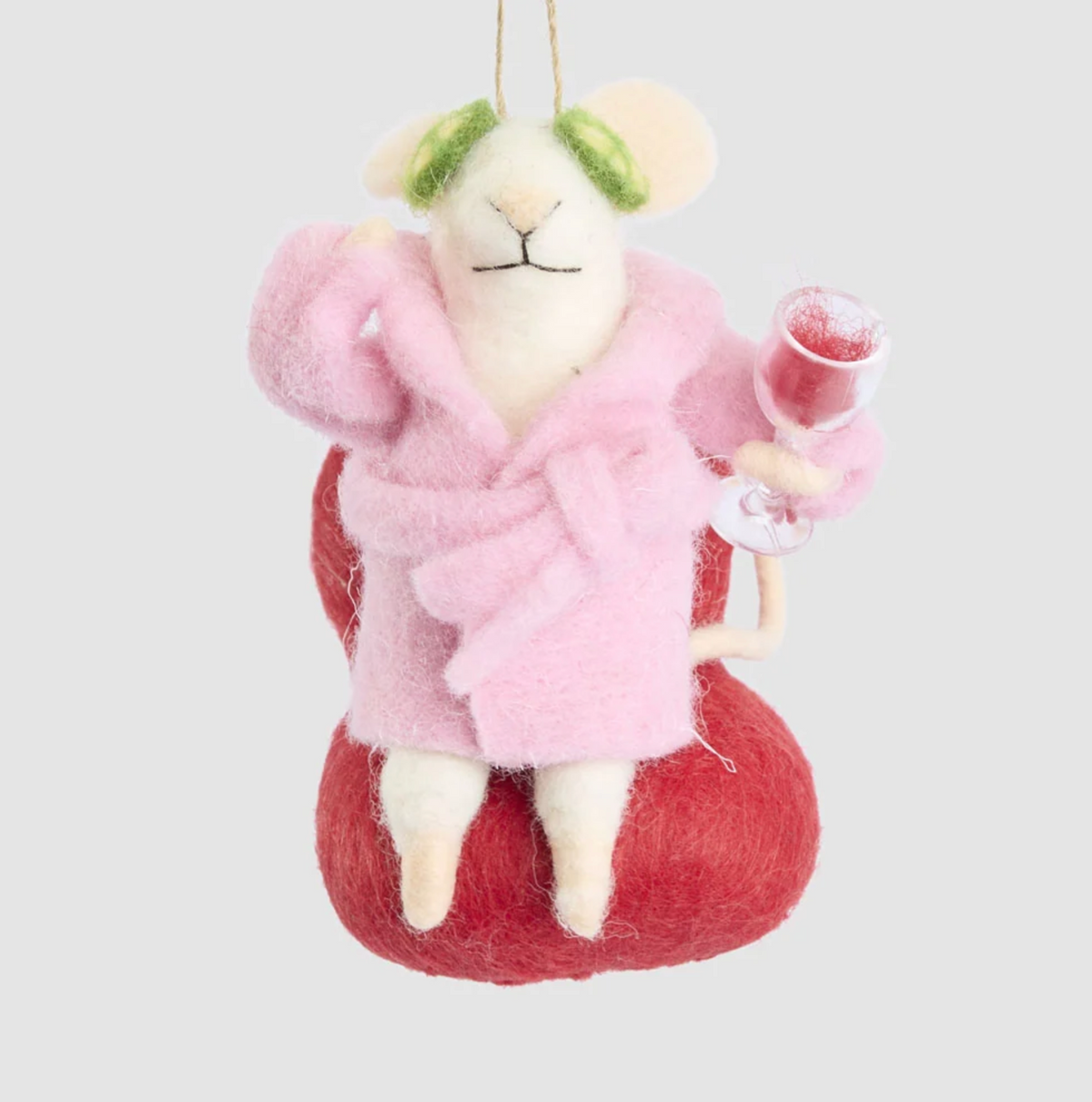 Cream mouse hanging decoration in a pink dressing gown, seated in a red chair with cucumber slices over its eyes and holding a wine glass