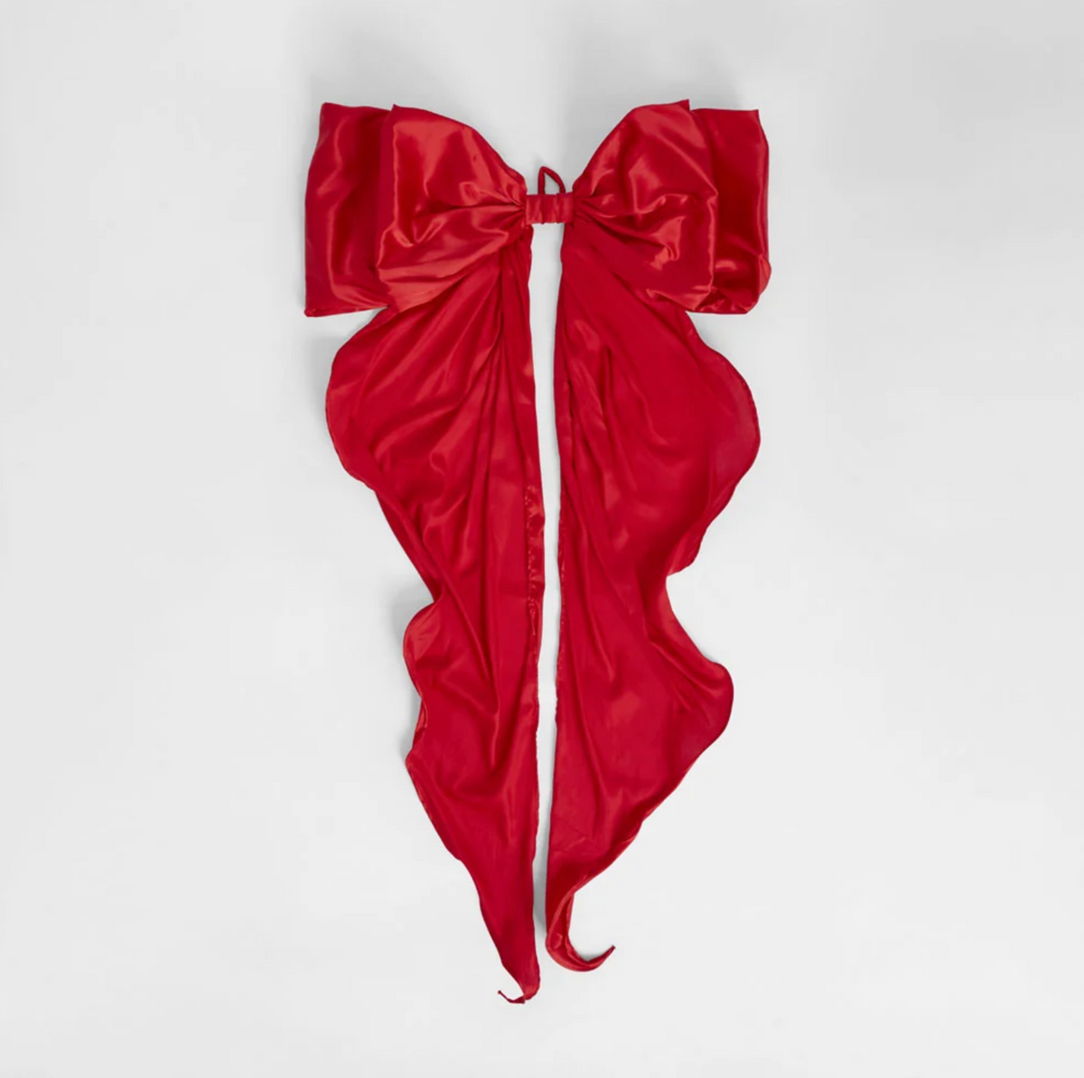 Scarlet red satin bow with broad loops and long curling tails against a plain background
