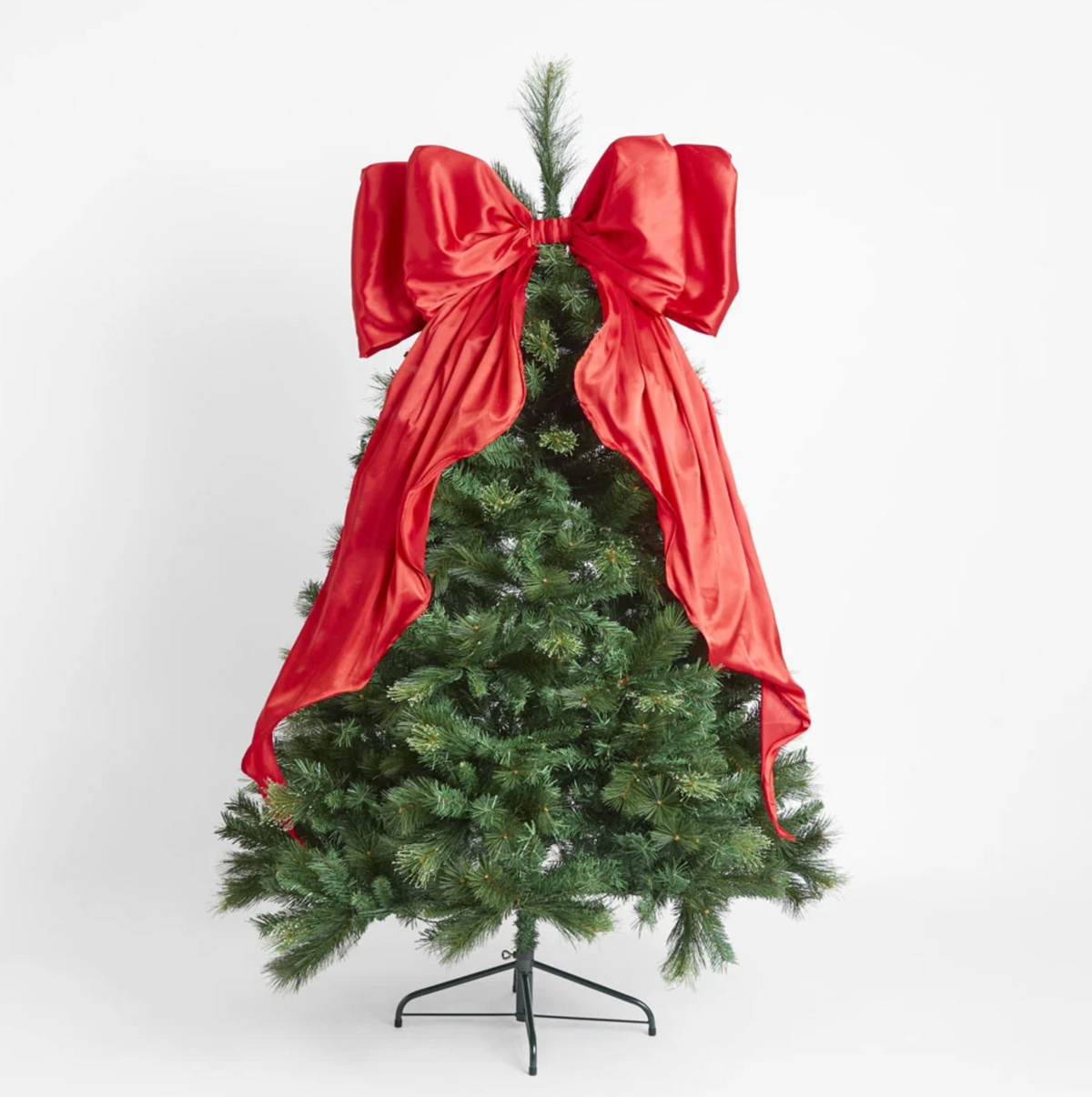 Red satin bow displayed at the top of a lit Christmas tree with long tails draped over the branches