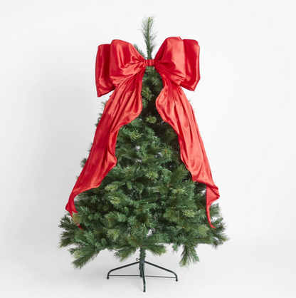 Red satin bow displayed at the top of a lit Christmas tree with long tails draped over the branches
