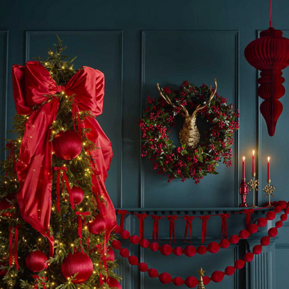 Red satin bow on a decorated Christmas tree beside a wreath and red garlands against a dark blue wall