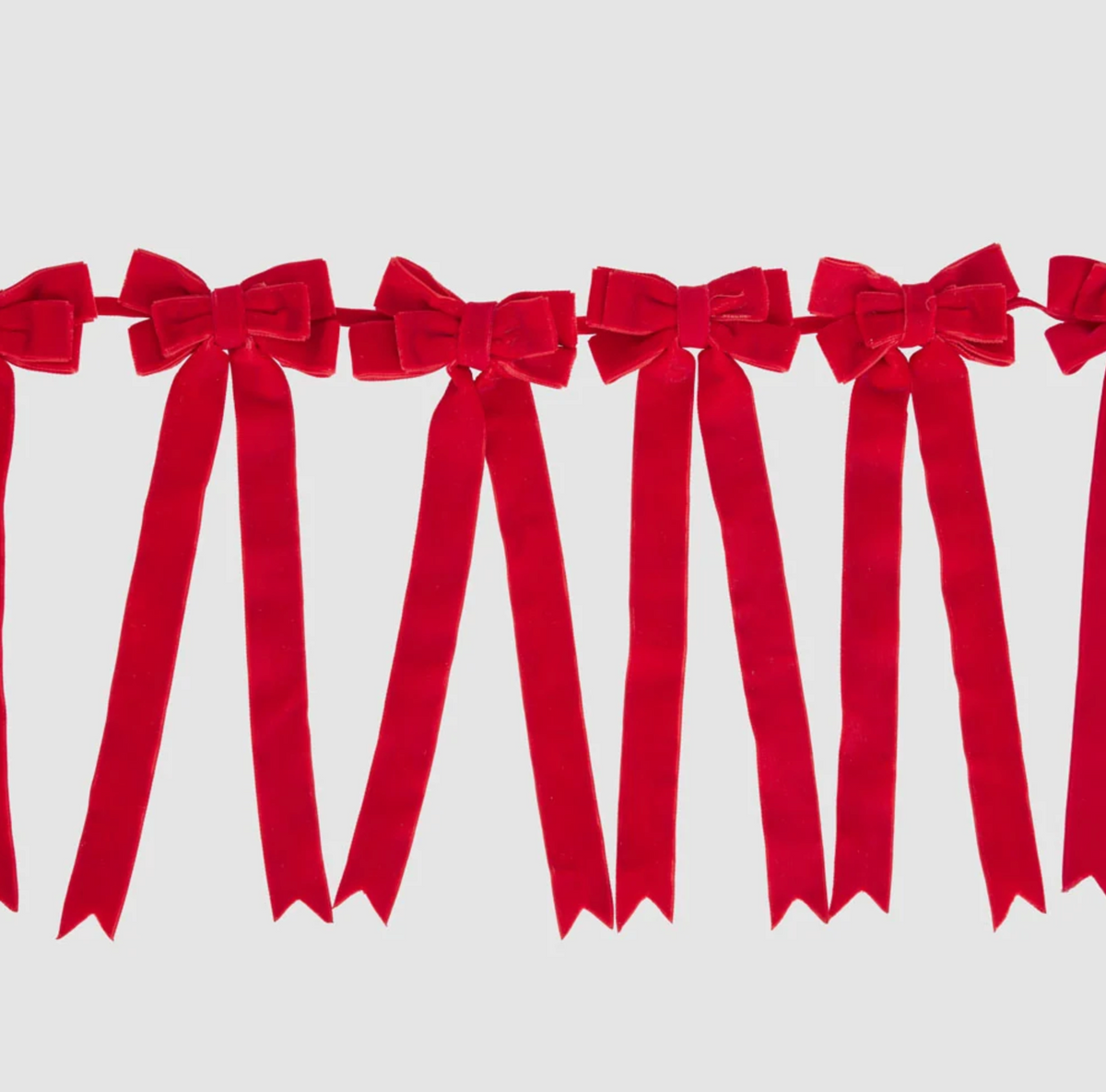 Red bow garland styled across a mantel in a Christmas display with a decorated tree, wreath and hanging ornaments