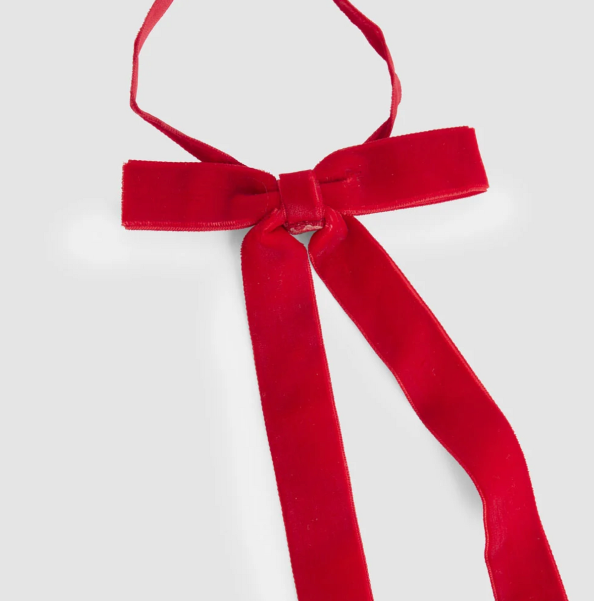 Red velvet tie-on bows arranged on a backing card with their long tails hanging down