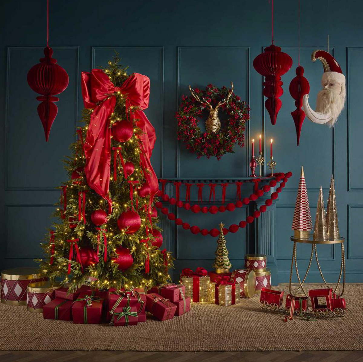 Santa moon decoration hanging beside red finials in a Christmas display with a decorated tree and gifts