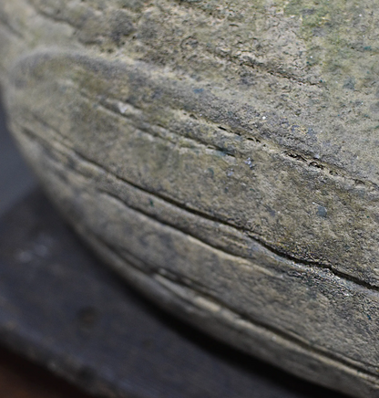Macro close-up of a textured stone or concrete surface with horizontal grooves and a dark base visible underneath.